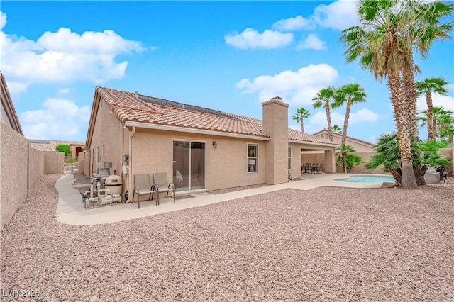 rear view of house featuring a tiled roof, a chimney, a patio area, and stucco siding