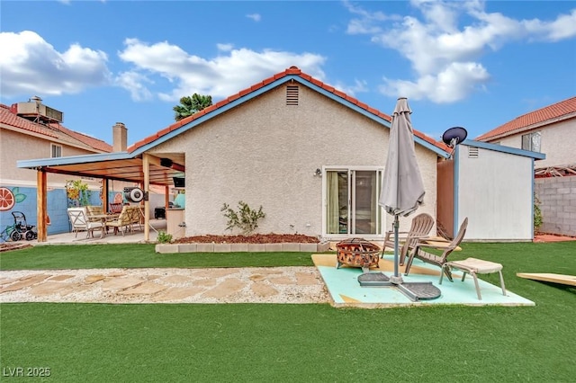 rear view of property featuring stucco siding, an outbuilding, a lawn, a patio, and a fire pit