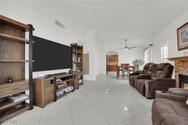 living area with arched walkways, a ceiling fan, light tile patterned floors, lofted ceiling, and visible vents