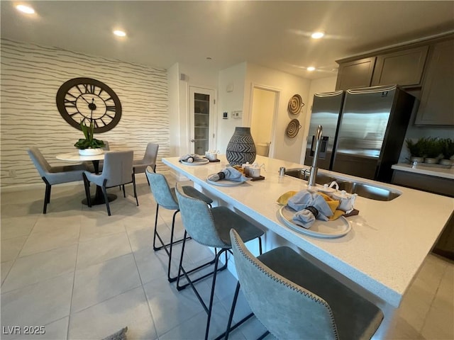 kitchen featuring stainless steel fridge, light countertops, a breakfast bar, and a sink