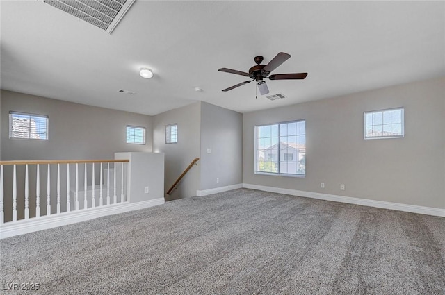 carpeted empty room featuring a ceiling fan, visible vents, and a wealth of natural light