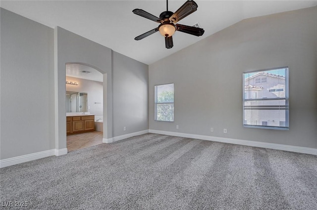 unfurnished bedroom featuring light colored carpet, arched walkways, baseboards, high vaulted ceiling, and ensuite bath