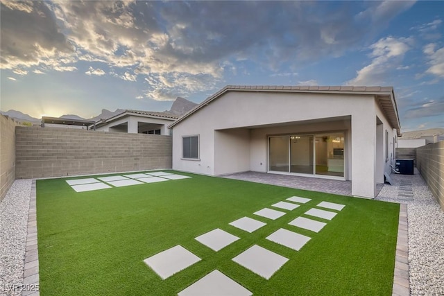 rear view of property featuring central AC, stucco siding, a fenced backyard, a patio area, and a lawn
