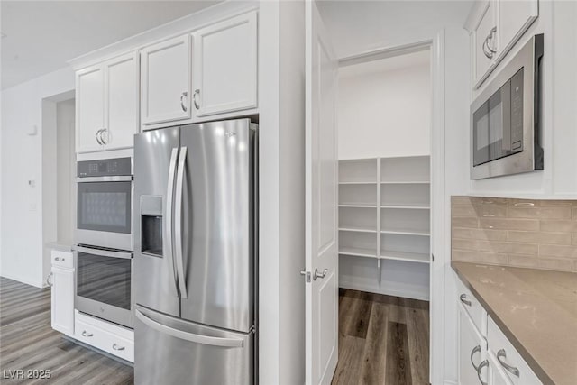 kitchen with backsplash, white cabinetry, light stone counters, stainless steel appliances, and light wood-style flooring