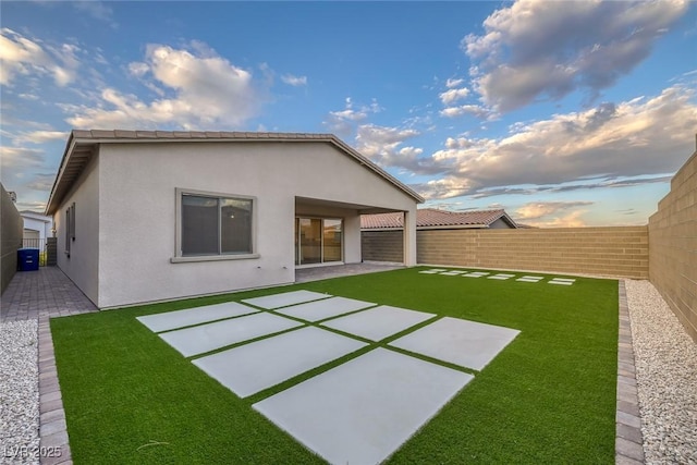 rear view of property with a yard, a fenced backyard, a patio area, and stucco siding