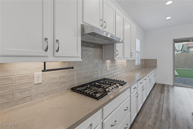 kitchen featuring decorative backsplash, wood finished floors, under cabinet range hood, white cabinets, and stainless steel gas stovetop