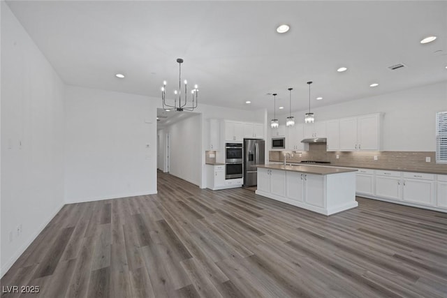 kitchen with wood finished floors, open floor plan, under cabinet range hood, a notable chandelier, and stainless steel appliances