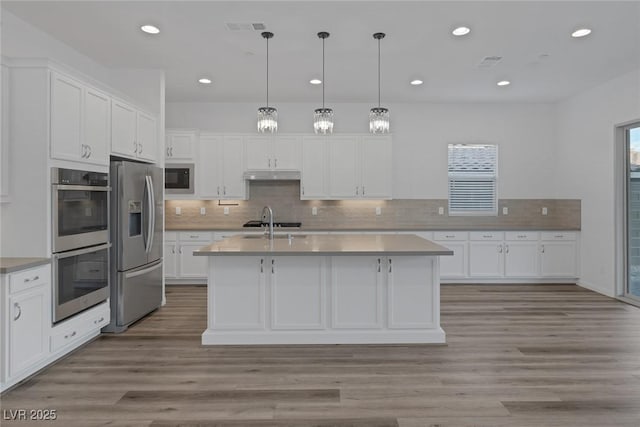 kitchen with light countertops, stainless steel appliances, white cabinetry, under cabinet range hood, and visible vents