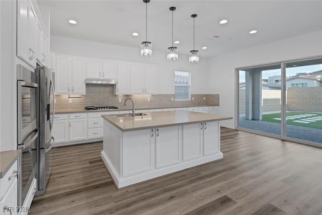 kitchen with dark wood-style flooring, appliances with stainless steel finishes, a sink, a kitchen island with sink, and backsplash