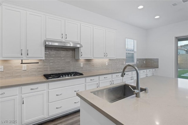 kitchen with white cabinets, a sink, stainless steel gas stovetop, under cabinet range hood, and visible vents