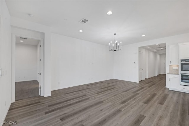 unfurnished dining area featuring visible vents, wood finished floors, baseboards, an inviting chandelier, and recessed lighting