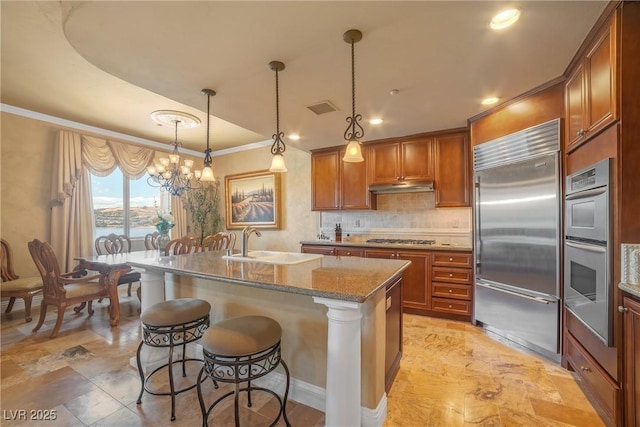 20 Via Mantova Unit 306, Henderson, NV 89011 - kitchen with appliances with stainless steel finishes, crown molding, under cabinet range hood, brown cabinetry, and backsplash
