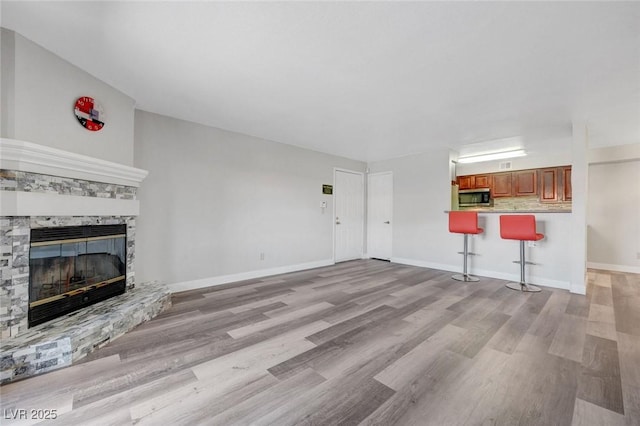 2451 N Rainbow Blvd Unit 2144, Las Vegas, NV 89108 - unfurnished living room featuring light wood-style floors, a stone fireplace, baseboards, and bar
