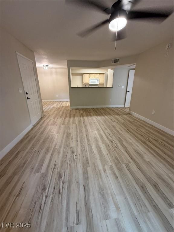 unfurnished living room featuring light wood-type flooring, a ceiling fan, baseboards, and visible vents