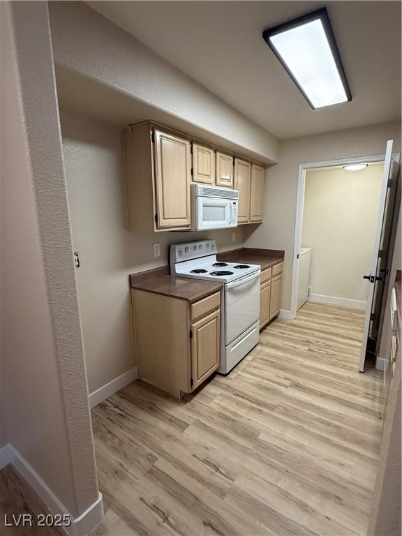 kitchen with light brown cabinets, dark countertops, white appliances, light wood-style floors, and baseboards