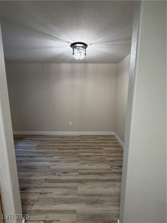 unfurnished room with baseboards, a textured ceiling, and wood finished floors