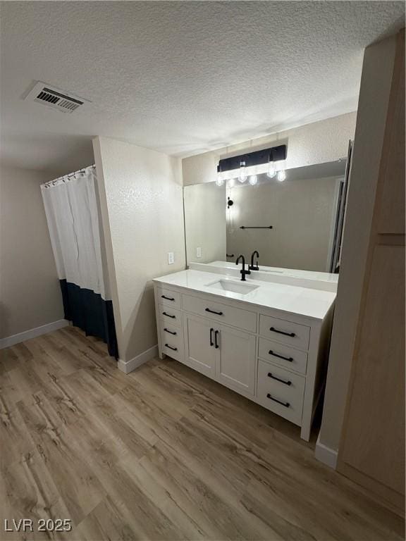 bathroom with visible vents, a textured ceiling, wood finished floors, and vanity
