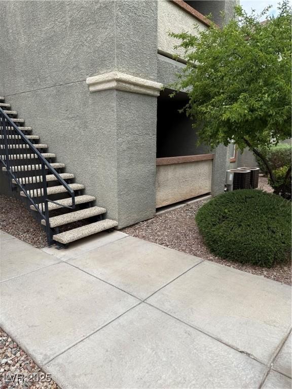 view of side of home featuring stucco siding, cooling unit, and stairway