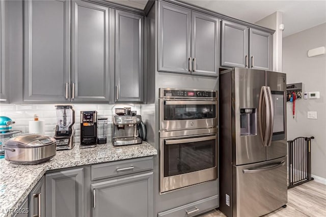39 Castleton Tower Ct, Henderson, NV 89011 - kitchen featuring light stone countertops, tasteful backsplash, light wood finished floors, gray cabinetry, and stainless steel appliances