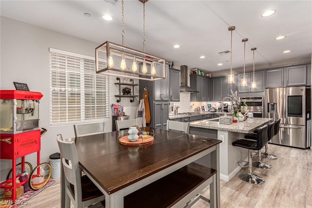 39 Castleton Tower Ct, Henderson, NV 89011 - kitchen featuring decorative backsplash, a center island with sink, light wood-type flooring, stainless steel appliances, and wall chimney exhaust hood
