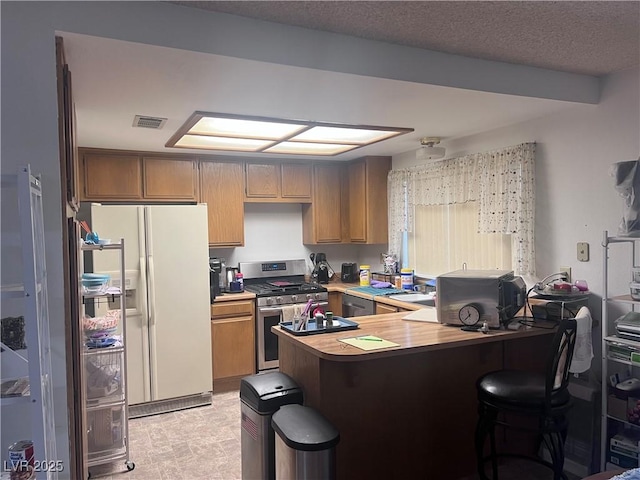 kitchen with stainless steel gas stove, white refrigerator with ice dispenser, a peninsula, and a kitchen breakfast bar