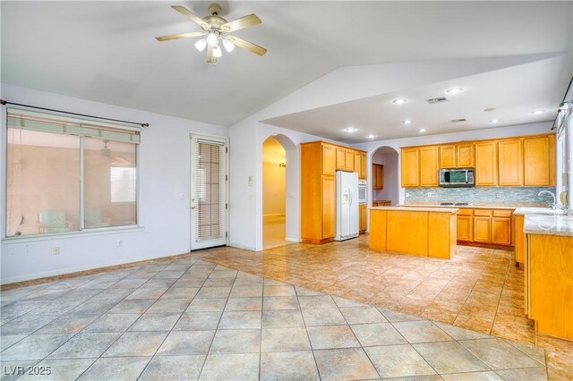 2383 Rainswept Ave, Henderson, NV 89052 - kitchen featuring a kitchen island, arched walkways, white refrigerator with ice dispenser, vaulted ceiling, and stainless steel microwave