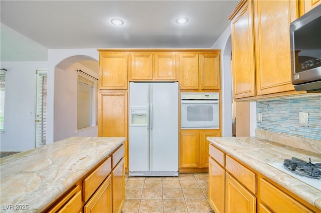 2383 Rainswept Ave, Henderson, NV 89052 - kitchen featuring light stone counters, white appliances, arched walkways, decorative backsplash, and light tile patterned floors