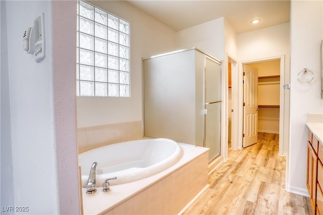 2383 Rainswept Ave, Henderson, NV 89052 - bathroom featuring a walk in closet, vanity, a shower stall, wood finished floors, and a garden tub