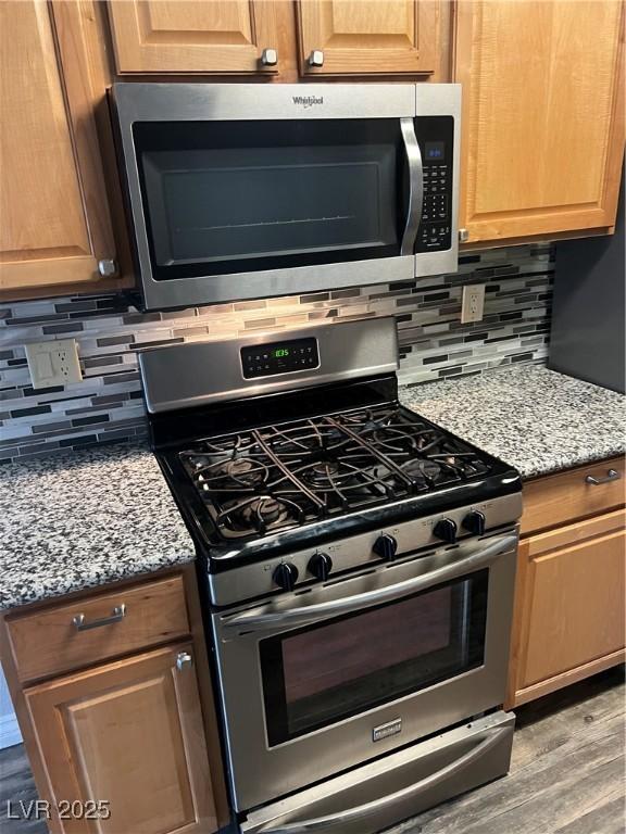 kitchen featuring tasteful backsplash, light stone countertops, stainless steel appliances, and light wood-style flooring