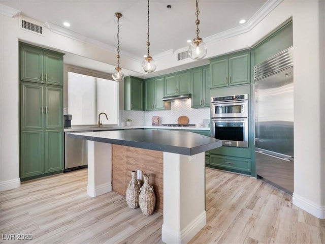 kitchen featuring light wood finished floors, appliances with stainless steel finishes, green cabinets, and ornamental molding