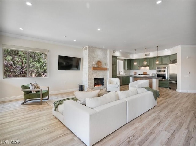 living room featuring recessed lighting, crown molding, baseboards, a stone fireplace, and light wood-style floors