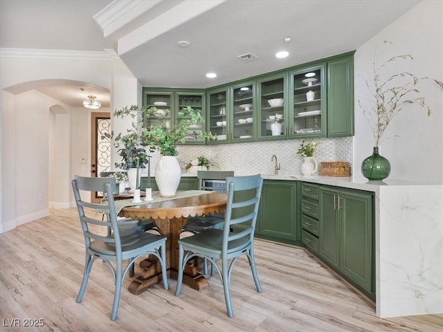 dining space featuring visible vents, crown molding, arched walkways, baseboards, and light wood-style floors