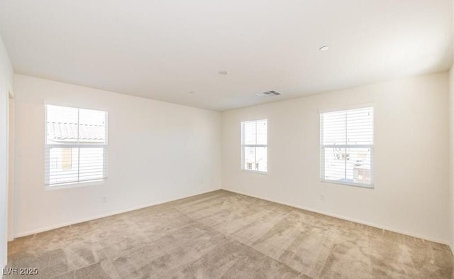 spare room featuring light colored carpet, visible vents, and baseboards