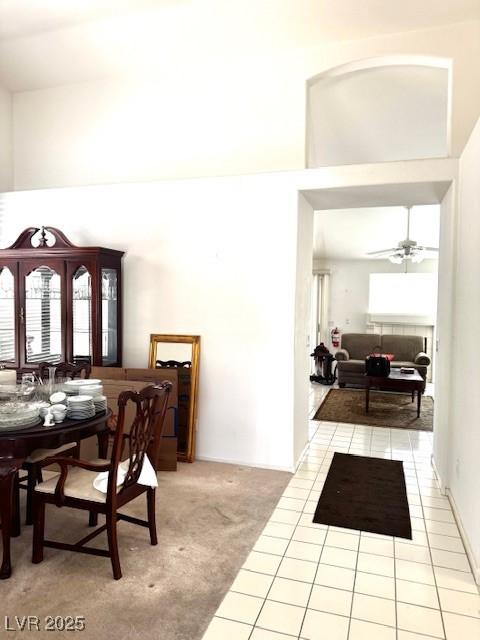 carpeted dining area featuring tile patterned flooring, a towering ceiling, and ceiling fan