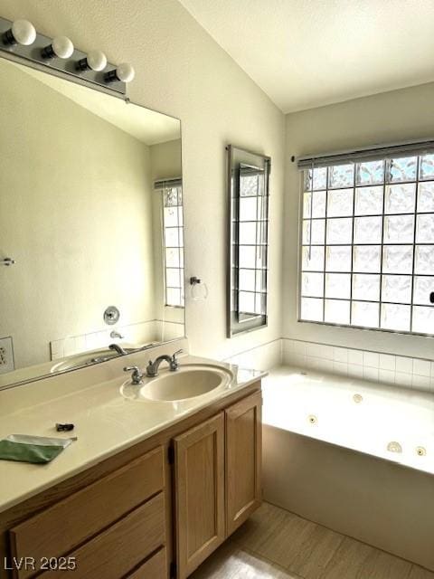 bathroom with vaulted ceiling, a whirlpool tub, vanity, and a healthy amount of sunlight