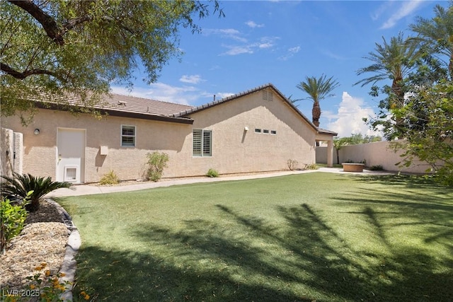 back of property with a lawn, stucco siding, a tile roof, and fence