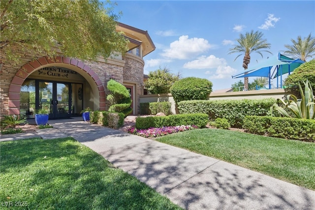 entrance to property featuring french doors, stone siding, and a lawn