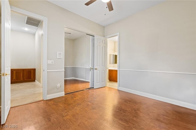 unfurnished bedroom with a ceiling fan, baseboards, ensuite bathroom, visible vents, and wood finished floors