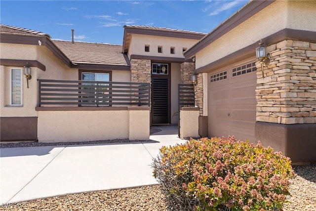 property entrance with stone siding, stucco siding, a tile roof, and a garage