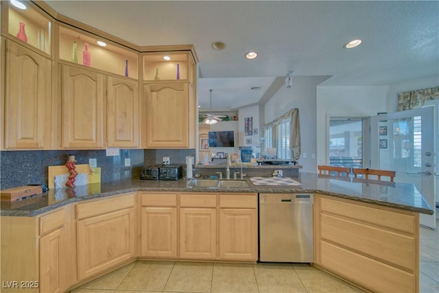 kitchen featuring a sink, a peninsula, dark stone countertops, dishwasher, and light brown cabinetry