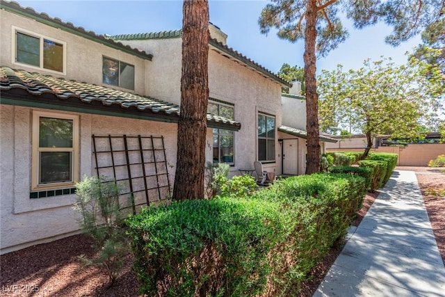 view of side of home featuring stucco siding, a tile roof, fence, and a chimney