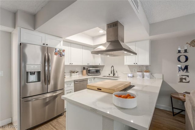 kitchen with a sink, a peninsula, island range hood, stainless steel appliances, and white cabinets