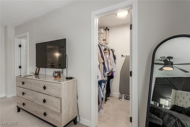 bedroom with a textured ceiling, baseboards, light colored carpet, and a walk in closet