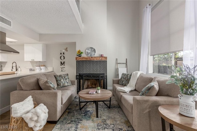 living area with a tiled fireplace, a textured ceiling, visible vents, and wood finished floors