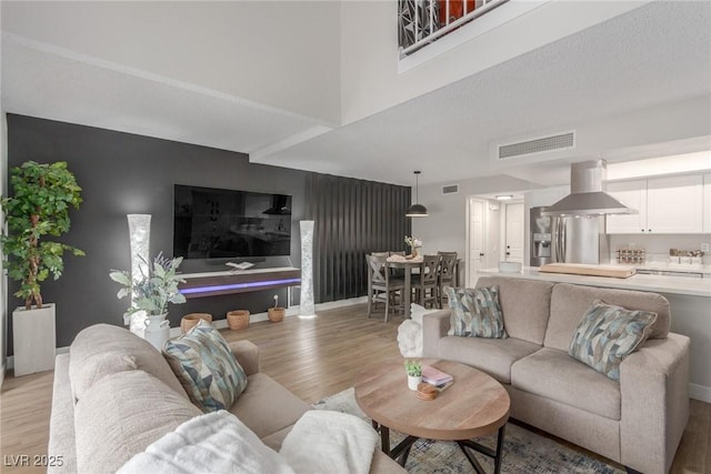 living area featuring light wood finished floors, visible vents, baseboards, and a towering ceiling