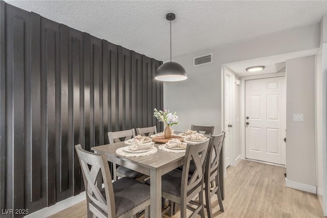dining room featuring baseboards, light wood-style flooring, visible vents, and a textured ceiling