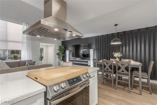 kitchen featuring light wood-type flooring, wall chimney exhaust hood, pendant lighting, white cabinetry, and stainless steel range with electric cooktop