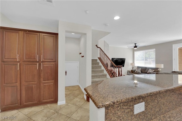 kitchen featuring stone countertops, brown cabinets, light tile patterned flooring, visible vents, and a ceiling fan