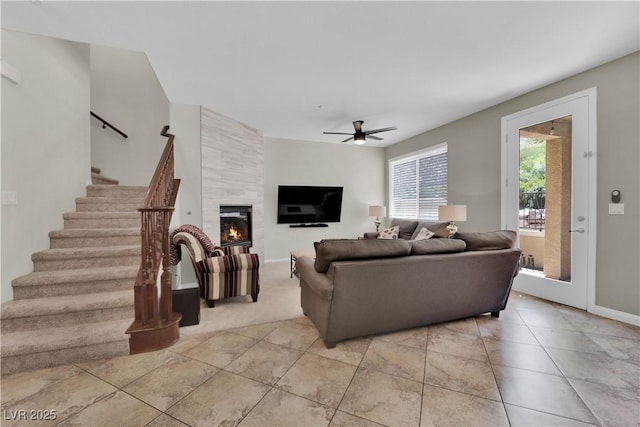 living room with a tile fireplace, light tile patterned floors, baseboards, ceiling fan, and stairway