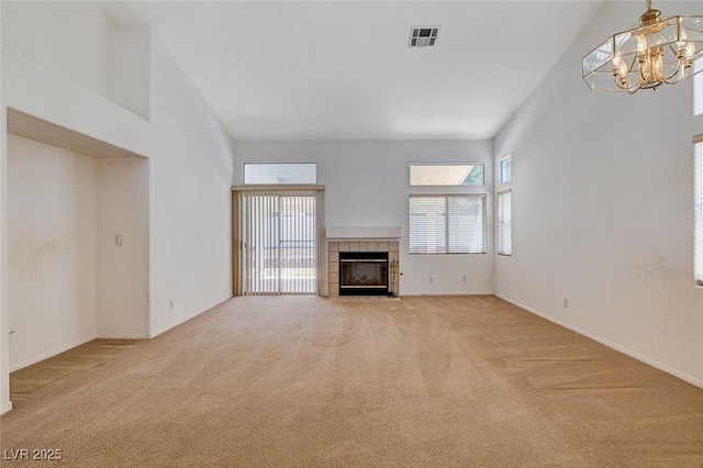 unfurnished living room featuring an inviting chandelier, a fireplace, baseboards, a towering ceiling, and light colored carpet